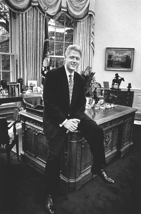 Bill Clinton sitting on the Resolute Desk in the Oval Office