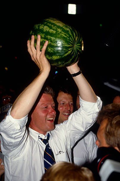 Bill Clinton holding a watermelon over his head in a crowd