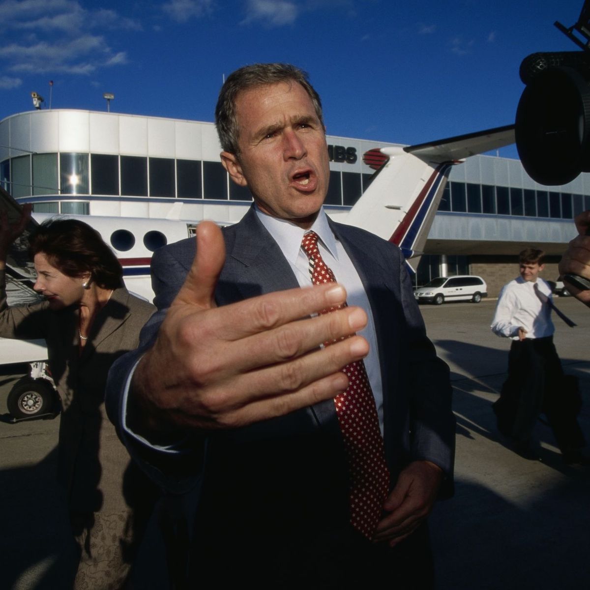 George W. Bush reaching toward a camera on an airport tarmac