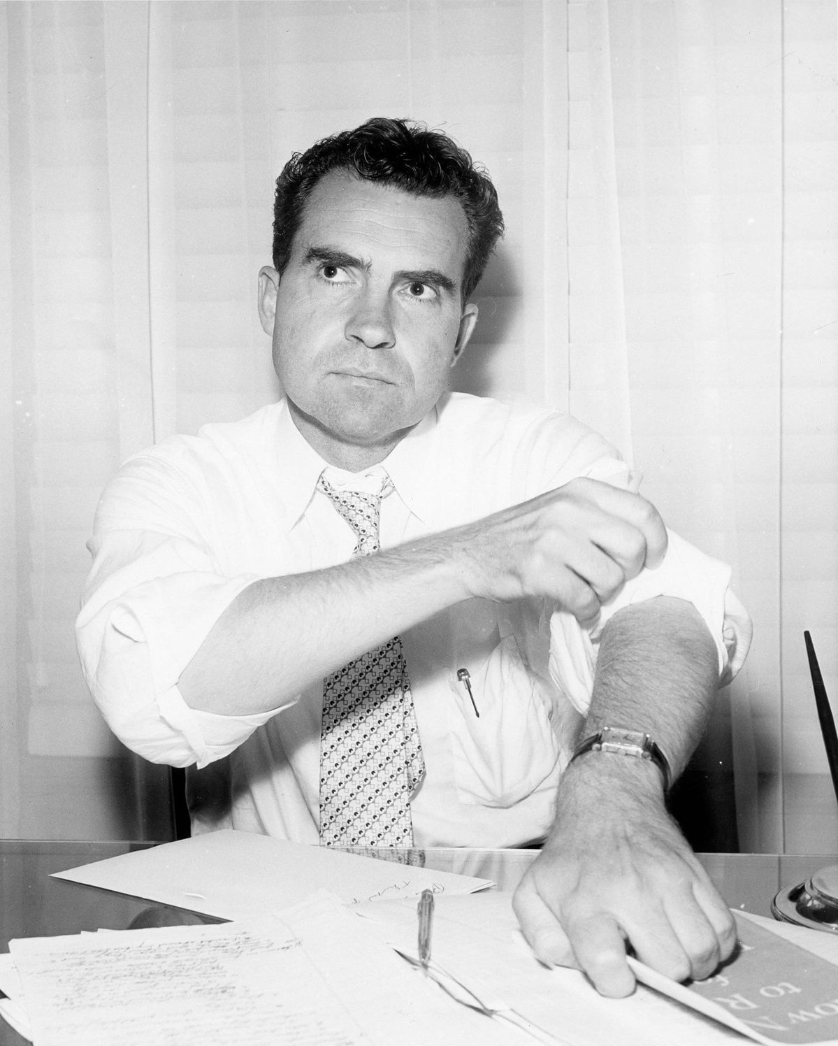 Richard Nixon rolling up his shirt sleeve at a desk